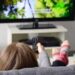 Person slapper av i sofaen og ser på TV med fjernkontrollen i hånden